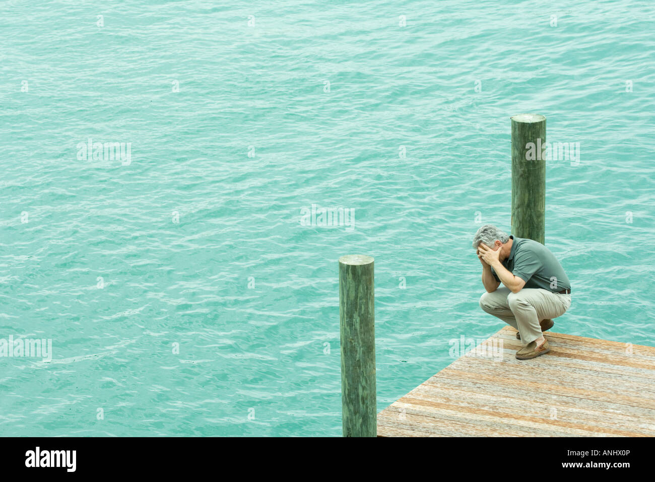 L'uomo accovacciato sul dock, tenendo testa, ad alto angolo di visione Foto Stock