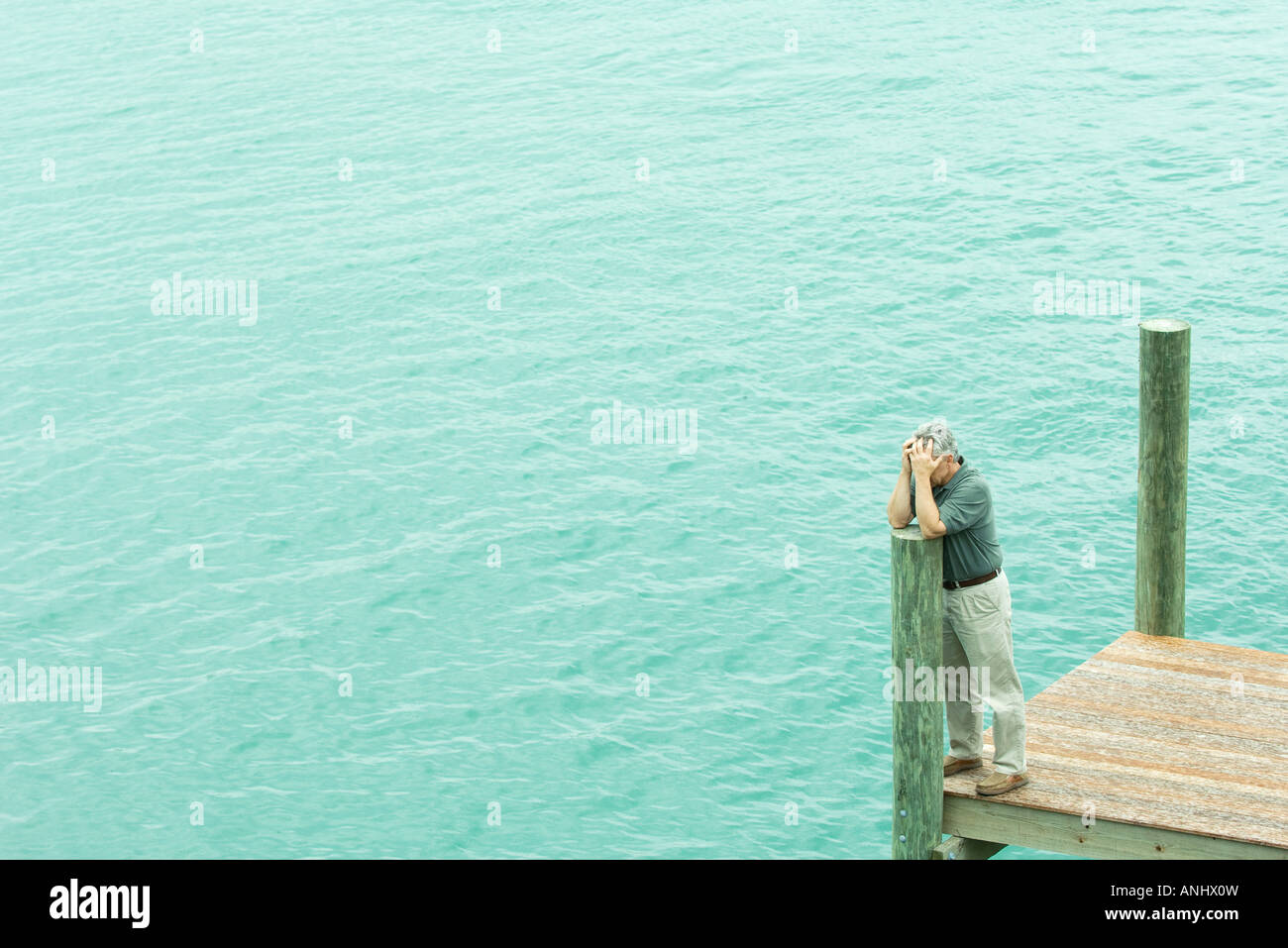 Uomo in piedi sul dock, appoggiata sul post, tenendo testa, ad alto angolo di visione Foto Stock
