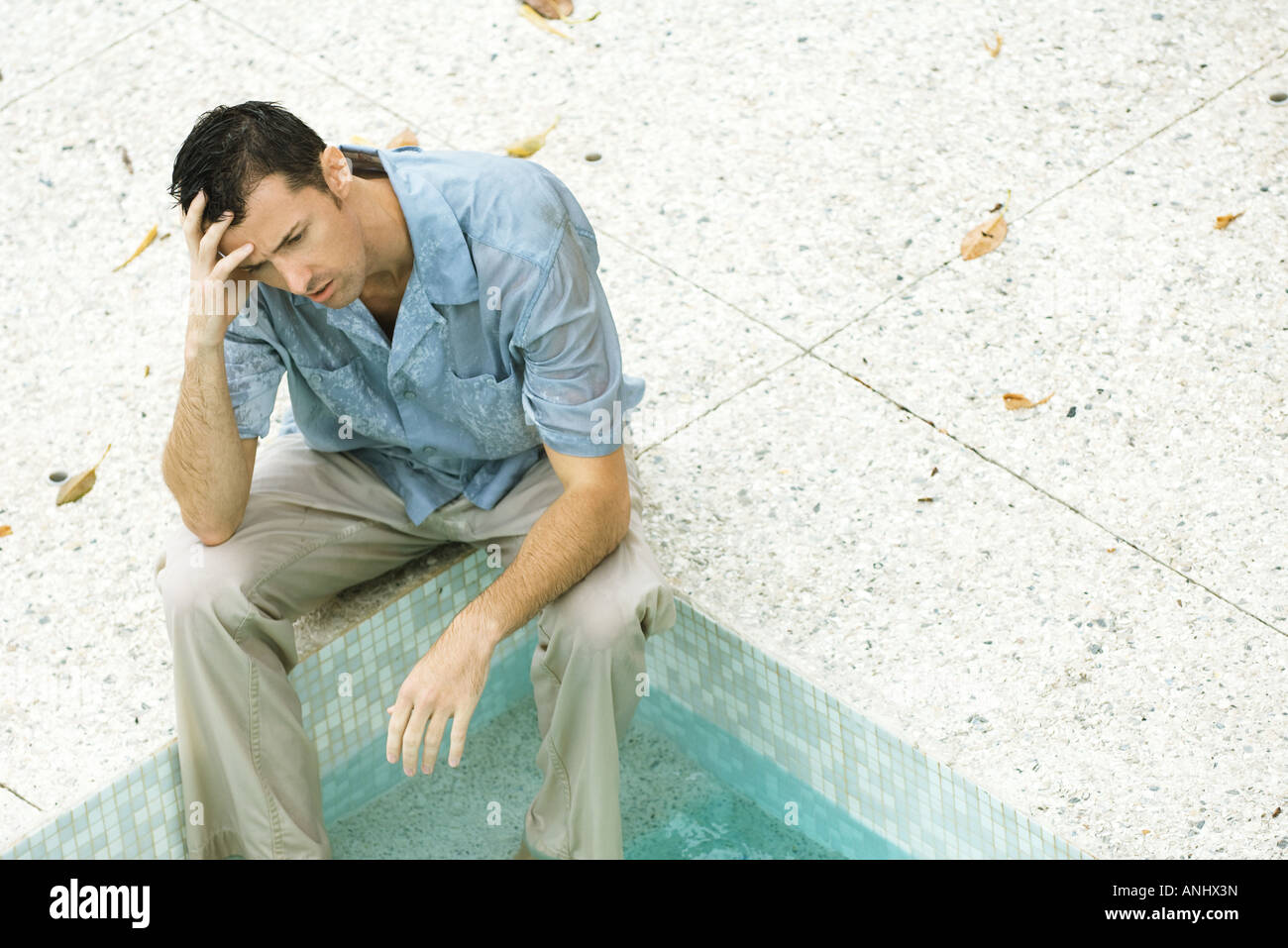 Uomo seduto con i piedi in piscina, tenendo testa, ad alto angolo di visione Foto Stock