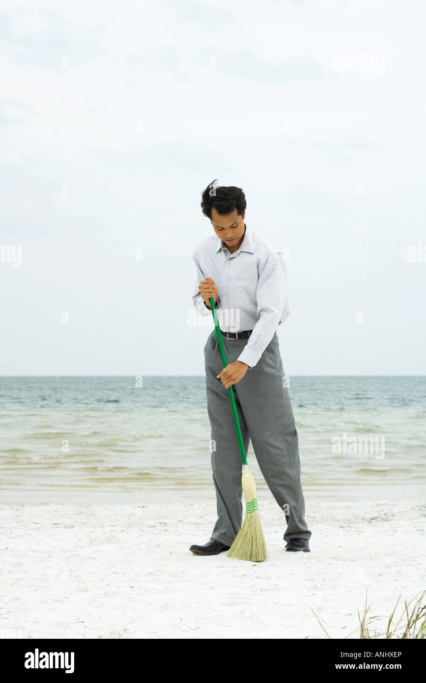 Uomo in piedi sulla spiaggia spazzare con la scopa a piena lunghezza Foto  stock - Alamy