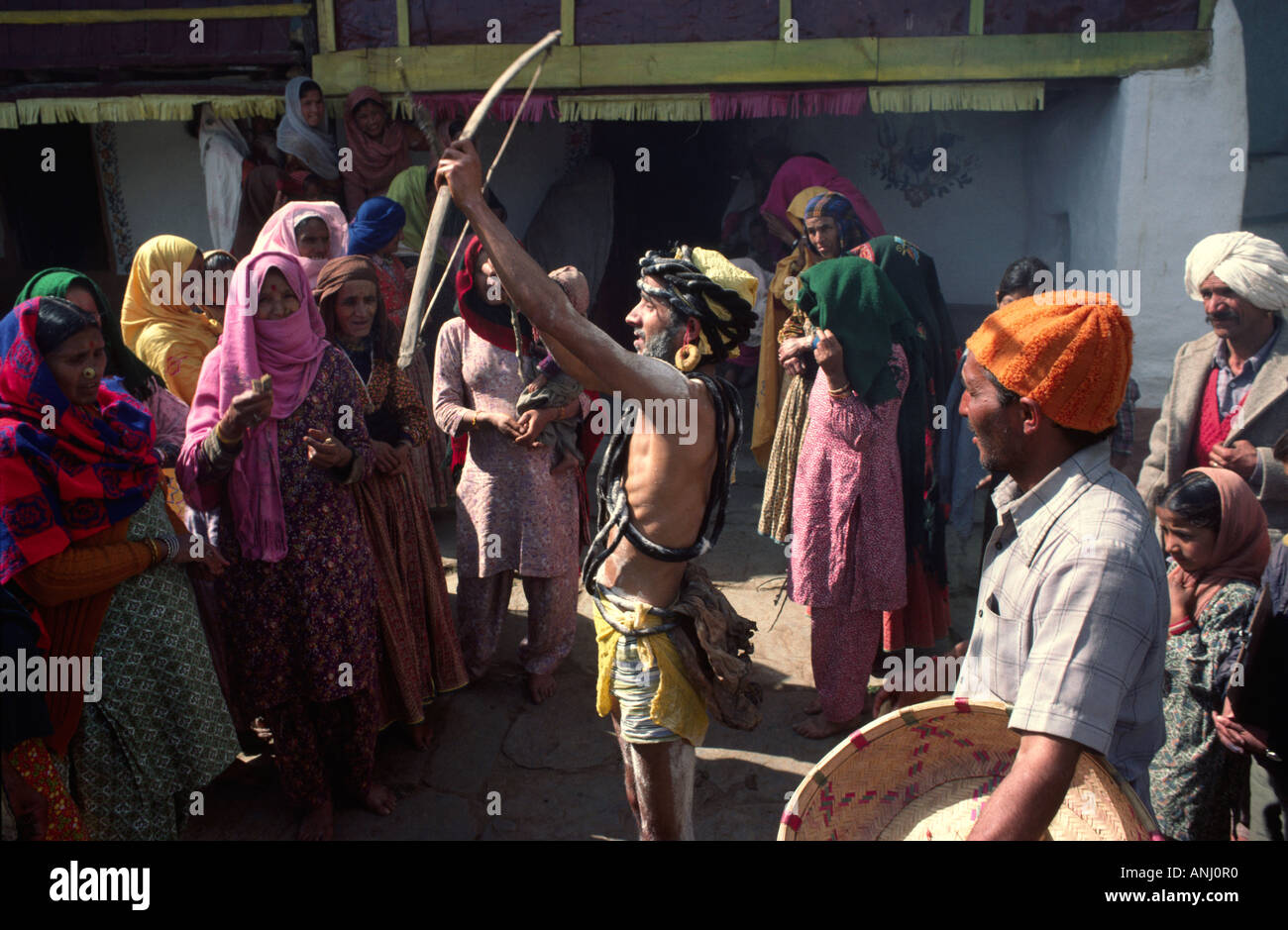 Sposo che esegue un rituale tradizionale con arco e freccia ad un matrimonio indù rurale nelle colline Himalayane di Himachal Pradesh, India Foto Stock