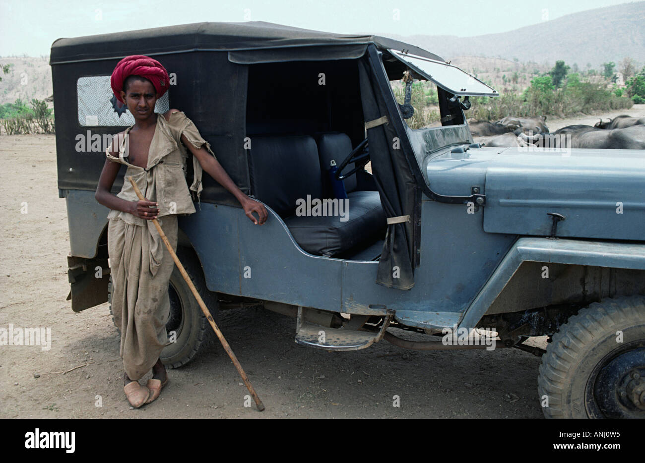 Un pastorello tradizionale della tribù nomade Rabari appoggiato contro una jeep per ombra in Gujarat, India Foto Stock