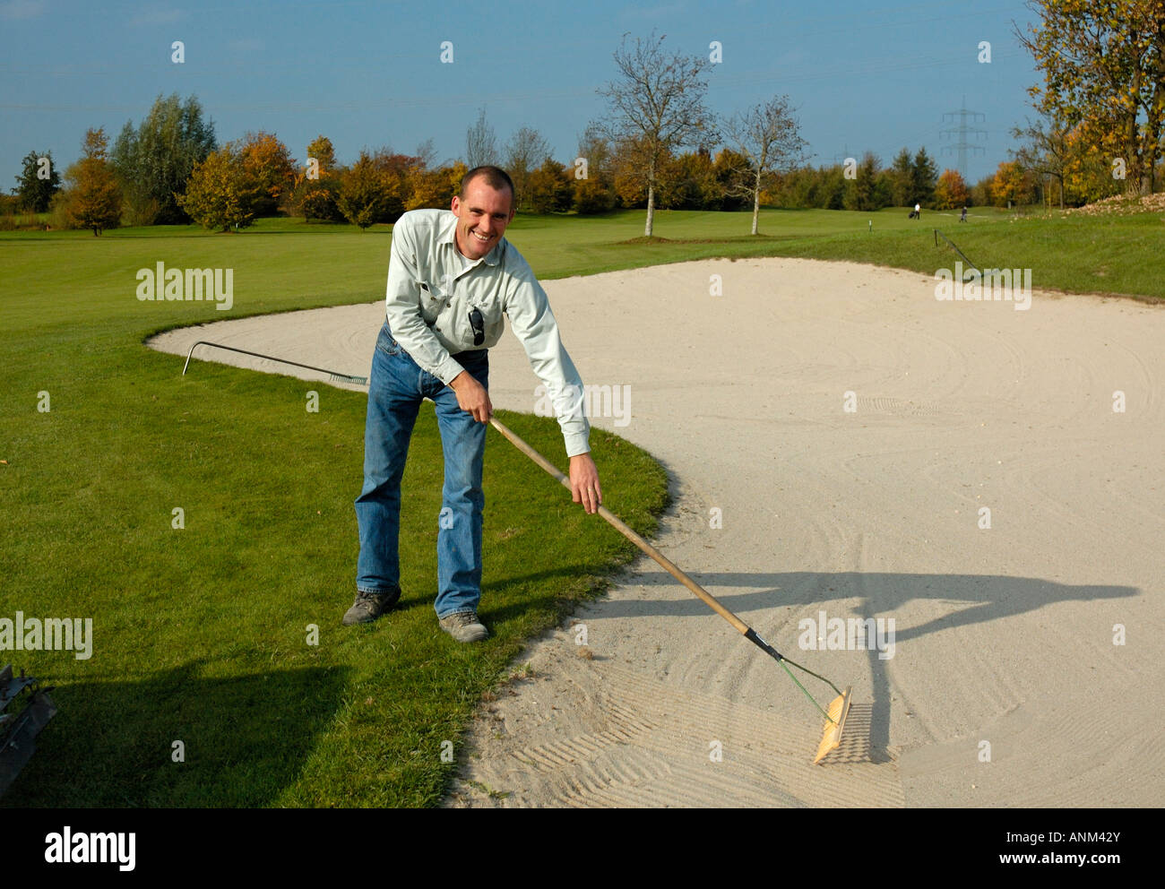 Capo Verde-keeper rastrellando sabbia nel bunker sul campo da golf. Foto Stock