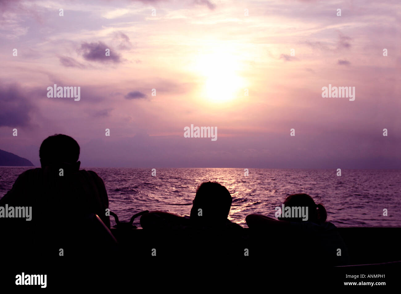 Silhouette di due uomini e una donna a guardare il mare delle Andamane e la regolazione del sole nel cielo da una nave Foto Stock