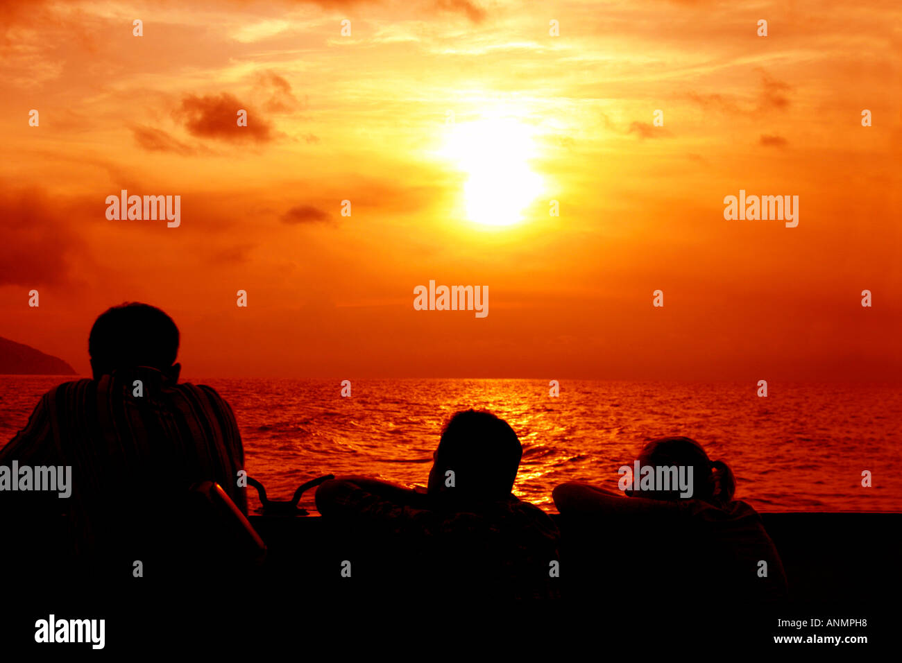 Silhouette di due uomini e una donna guarda la tinta oro sul Mare delle Andamane e il cielo al tramonto da una nave Foto Stock
