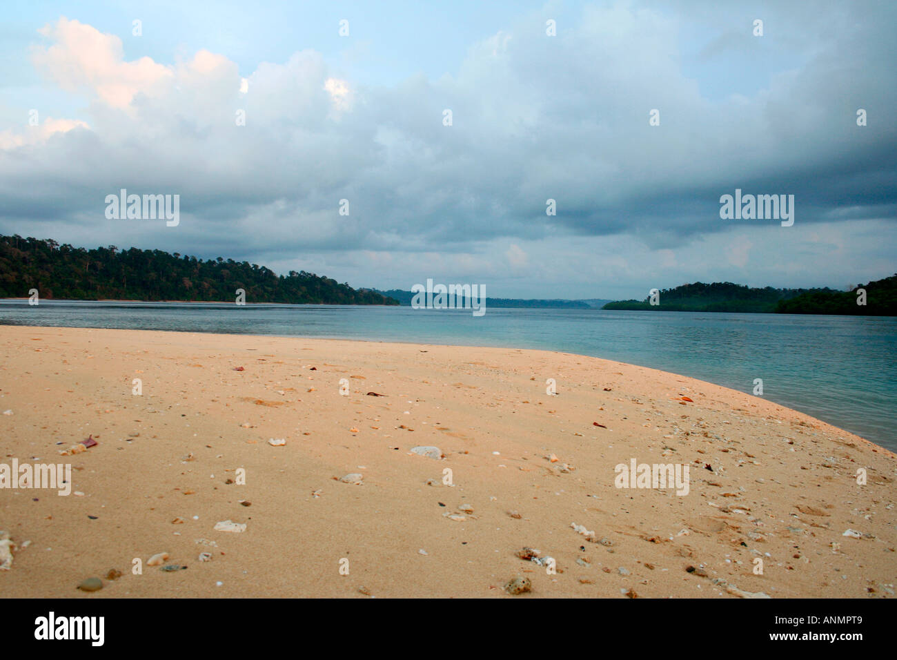 Un semi circolare vista di una spiaggia di Andamane e le acque del mare costeggiata da colline verdi contro un cielo velato al crepuscolo Foto Stock