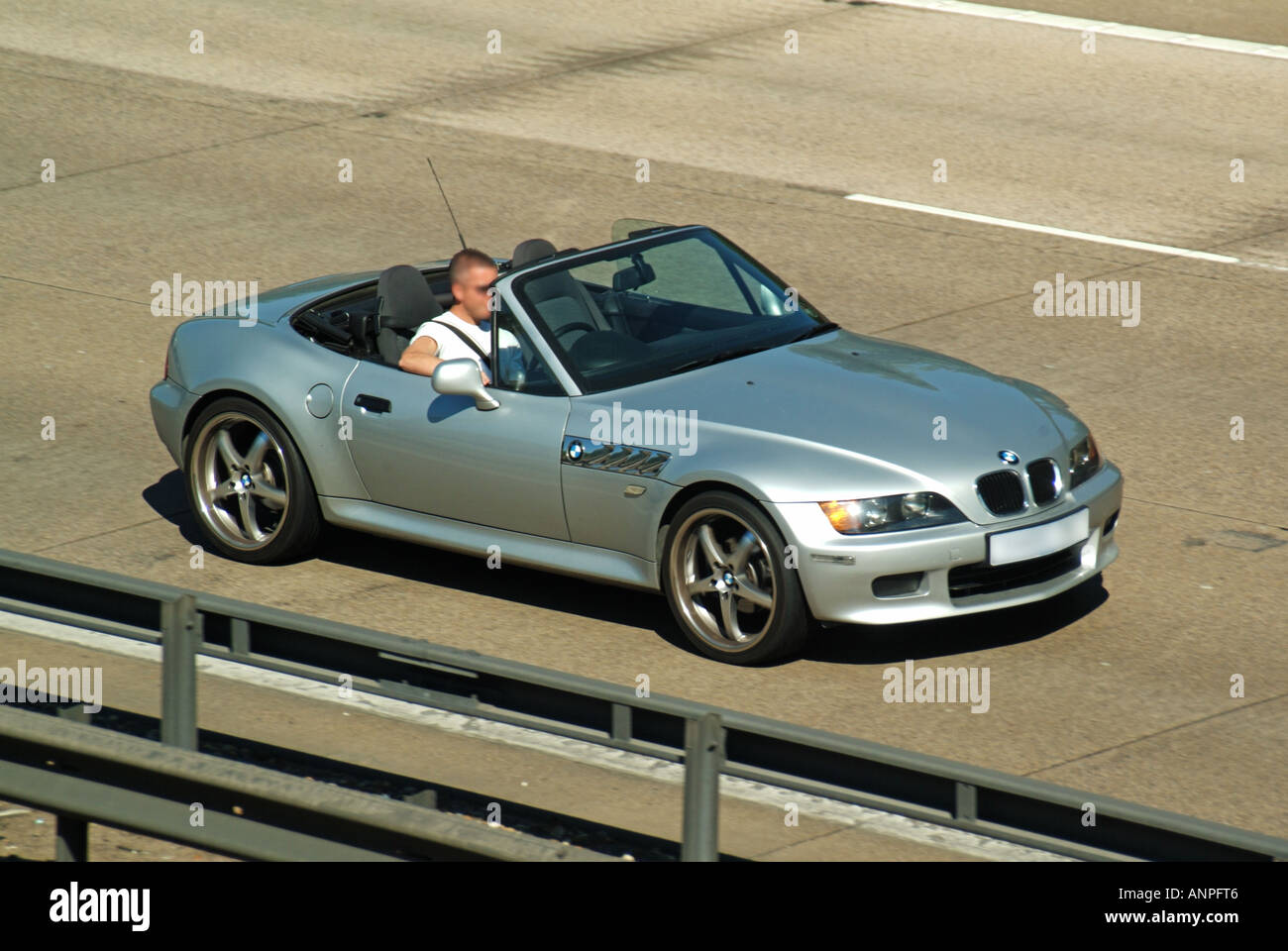 Vista estiva dall'alto lato e frontale guardando dall'alto uomo guida open top argento BMW capote auto giù oscurata targa autostrada Inghilterra Regno Unito Foto Stock