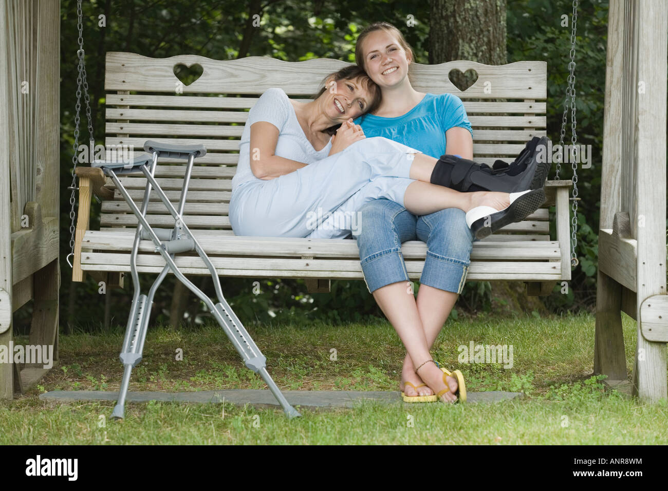 Donna di mezza età con lesioni e sua figlia seduta su un altalena e sorridente Foto Stock