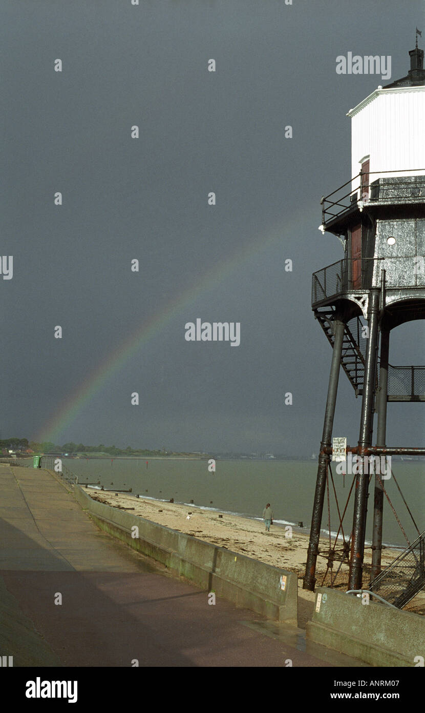 Arcobaleno nel cielo scuro dopo la tempesta con faro sulla riva del mare Foto Stock