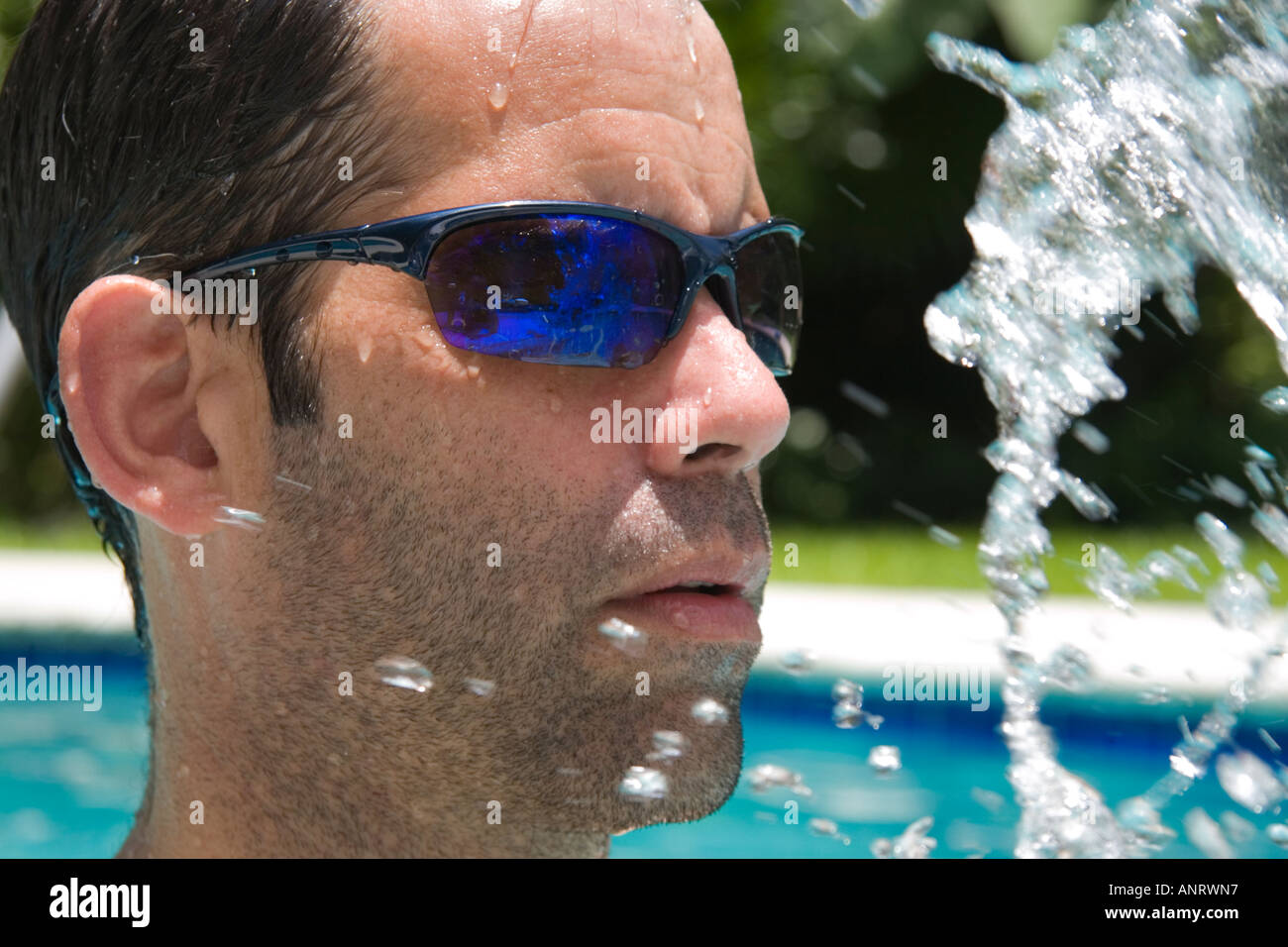 Un uomo che indossa gli occhiali da sole gli schizzi in una piscina Foto Stock