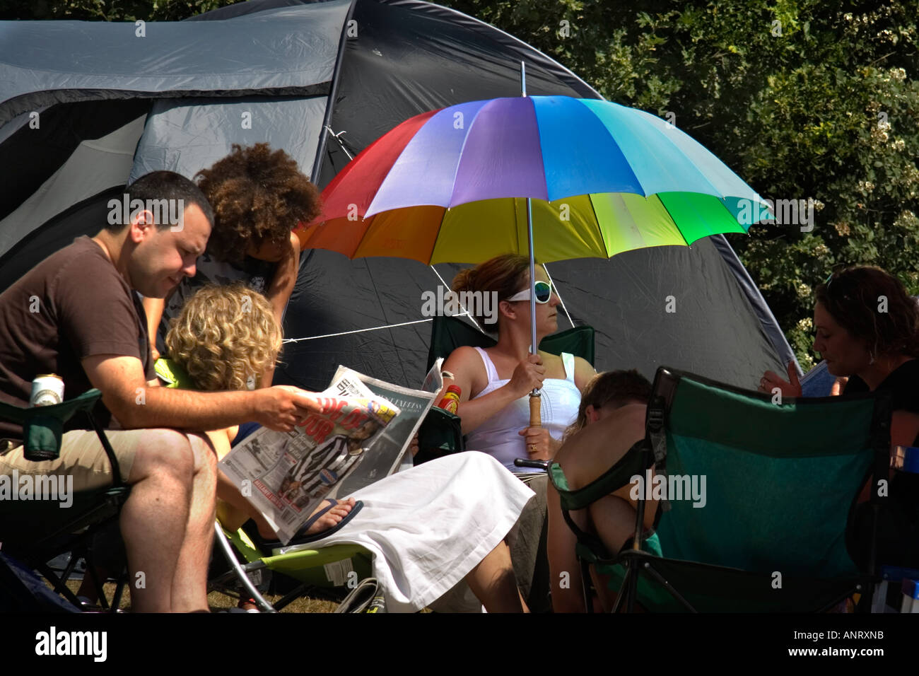 Una donna seduta con i suoi amici in un momento di relax a un campeggio azienda molto ombrello coloratissimo Foto Stock