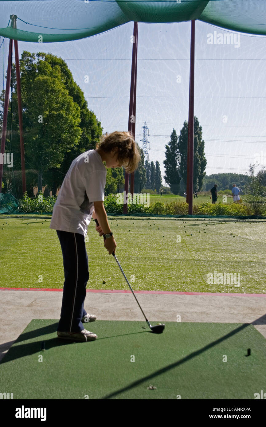Ragazzo giovane affrontare la sfera praticando il suo swing del golf in una gamma di guida Foto Stock