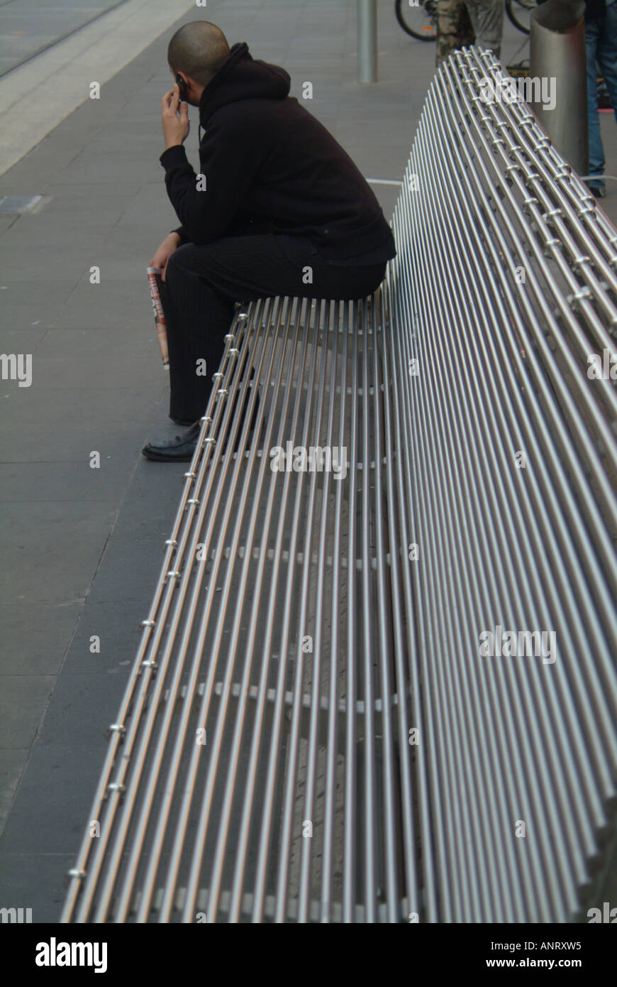 Un uomo solitario utilizzando un telefono cellulare su un banco in acciaio Foto Stock