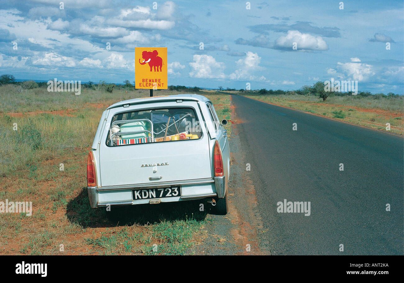 Peugeot 404 station wagon parcheggiata sul principale di Nairobi Mombasa road accanto a un cartello stradale la lettura ATTENZIONE ELEPHANT Kenya Africa orientale Foto Stock