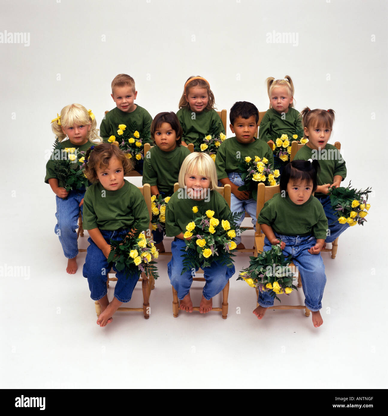 Dieci bambini in camicie verdi con un bouquet di fiori gialli seduti su sedie Foto Stock