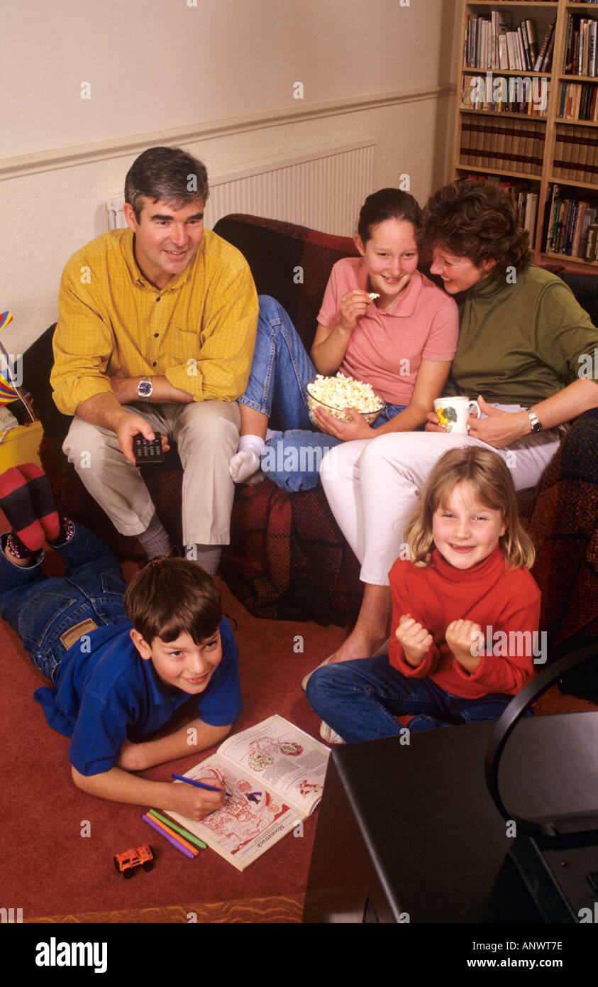 la famiglia di cinque anni '90 a casa è felicemente seduta insieme guardando la televisione nella loro stanza di famiglia. Home TV tradizionale degli anni '90 per famiglie Foto Stock