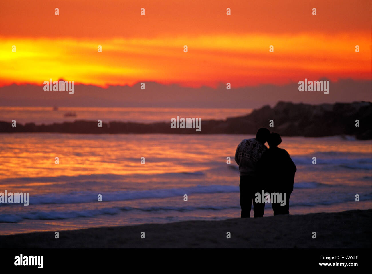 2 paio di due persone che si tengono per mano delle coccole di ogni altro a guardare il tramonto sulla spiaggia con onde che si infrangono sulla spiaggia spagna Foto Stock
