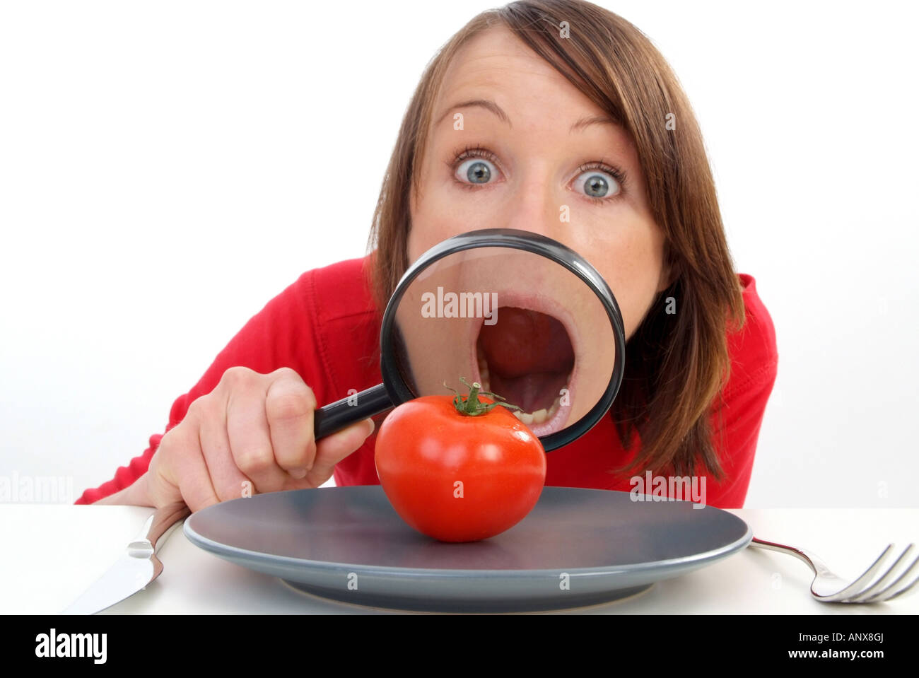 Giovane donna con lente di ingrandimento visto il pomodoro in corrispondenza della piastra Foto Stock