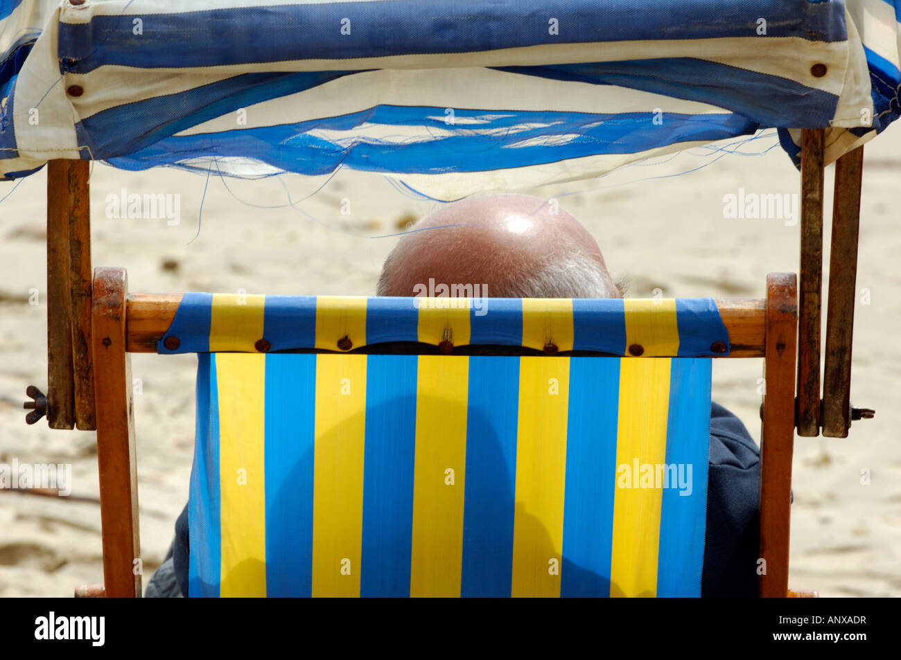 Un vecchio uomo o pensionato anziano gentiluomo seduto in una sedia a sdraio in spiaggia al sole con una testa calva Foto Stock