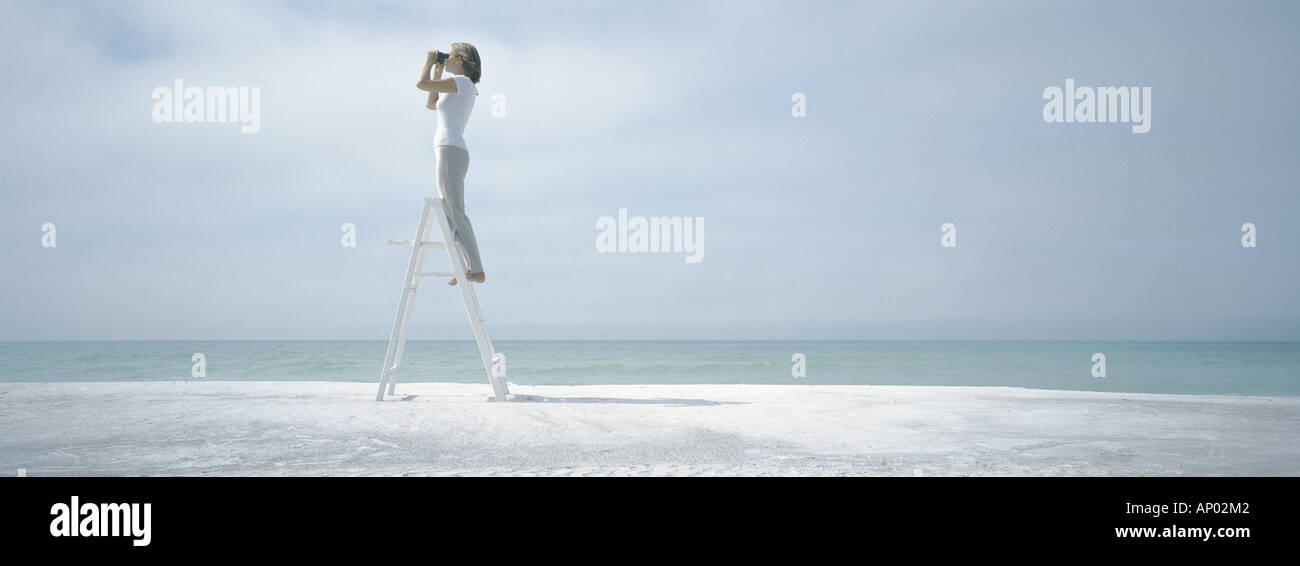 Donna in piedi sulla scala, guardando attraverso il binocolo, sulla spiaggia Foto Stock