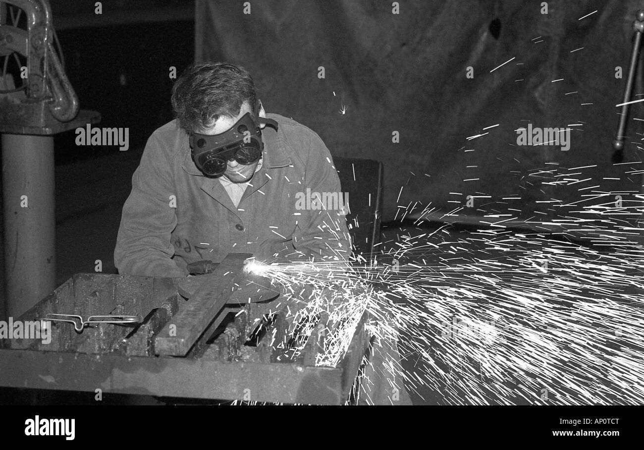 Uomo con occhiali di protezione utilizzando gas propano pistola di masterizzazione per il taglio di barre di acciaio. Foto Stock