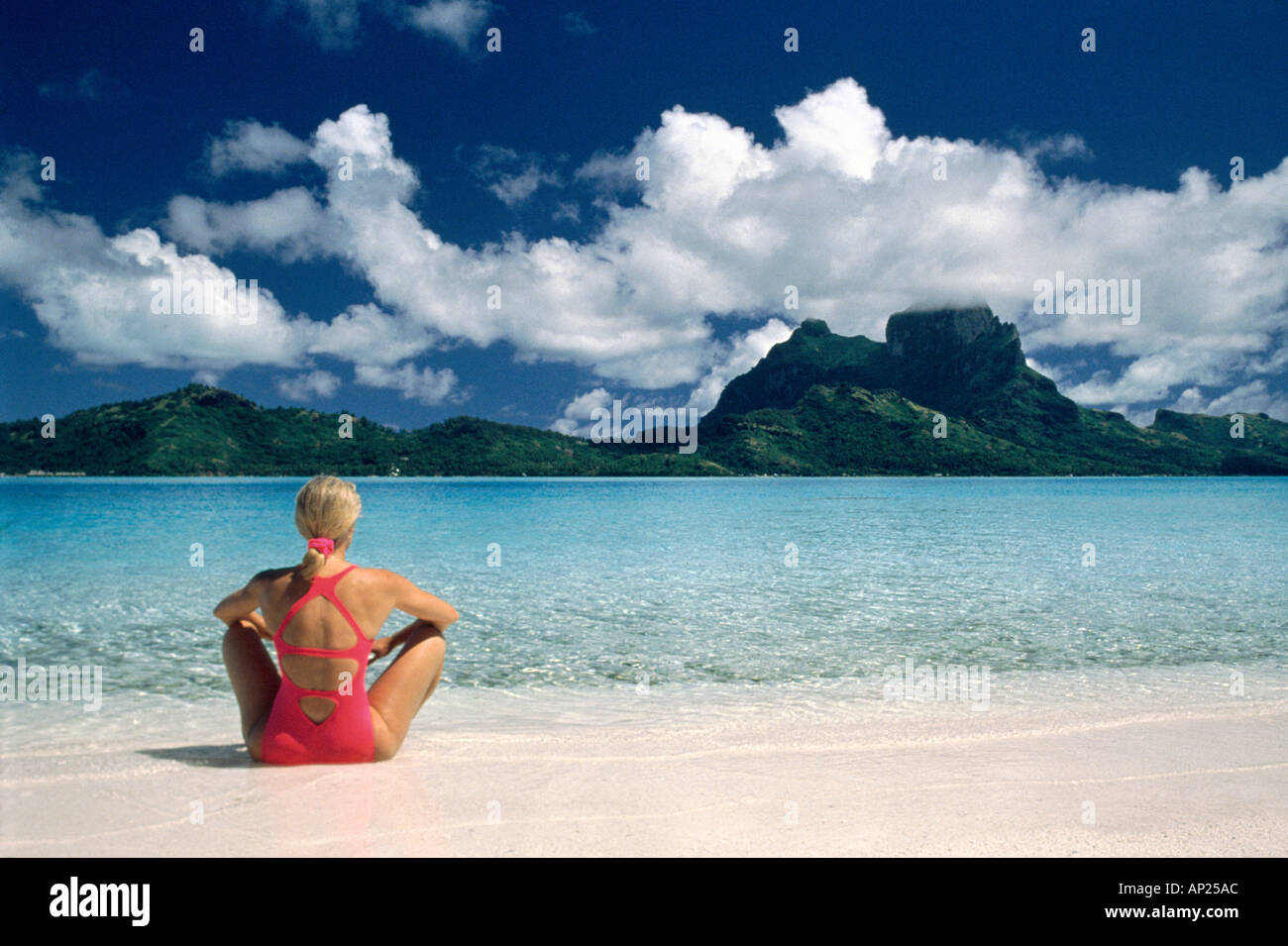 Donna seduta sulla spiaggia di sabbia bianca con un cielo blu e nuvole Foto Stock