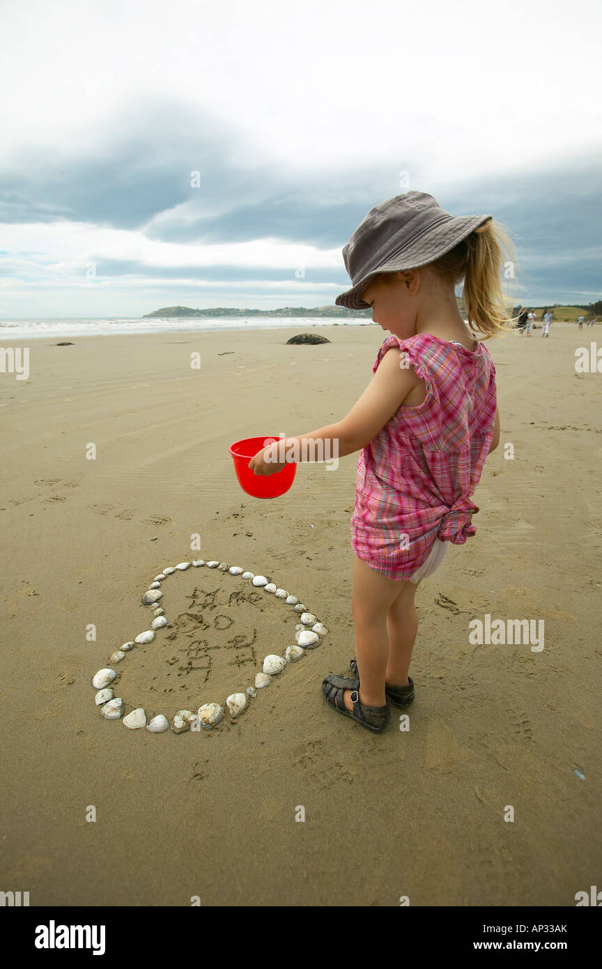Ragazza ad esplorare il cuore realizzato da conchiglie, spiaggia con massi Moeraki, a sud di Oamaru, Eastcoast, Isola del Sud, Nuova Zelanda Foto Stock