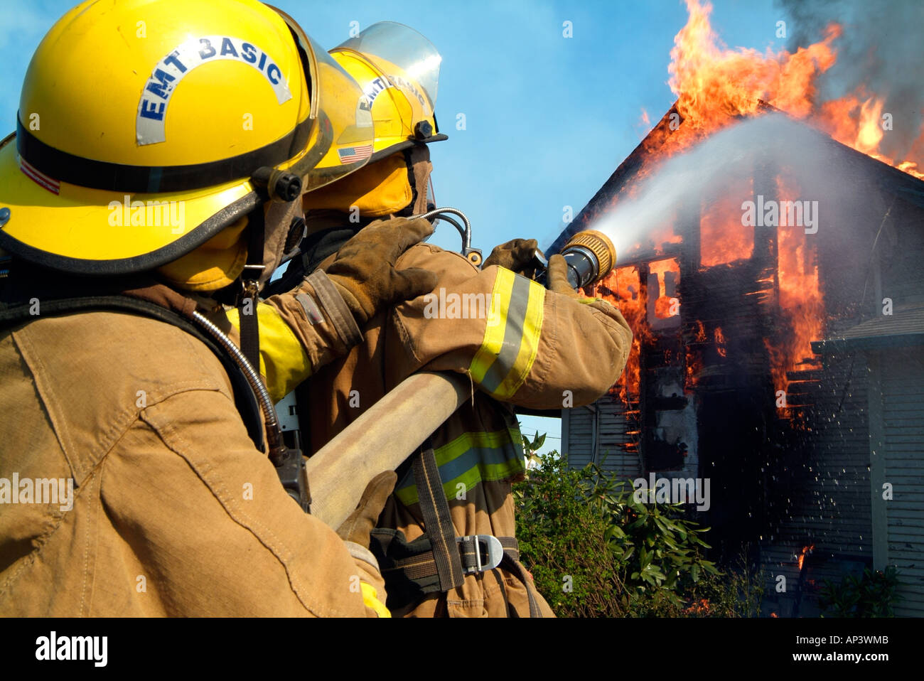 Due vigili del fuoco versare l'acqua su un inferno, il tentativo di abbattere le fiamme che stanno consumando una casa. Foto Stock