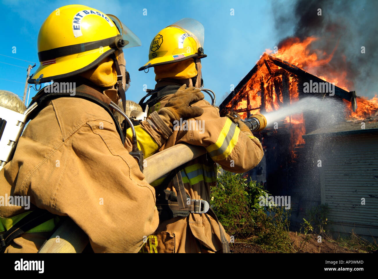 Due vigili del fuoco versare l'acqua su un inferno, il tentativo di abbattere le fiamme che stanno consumando una casa. Foto Stock