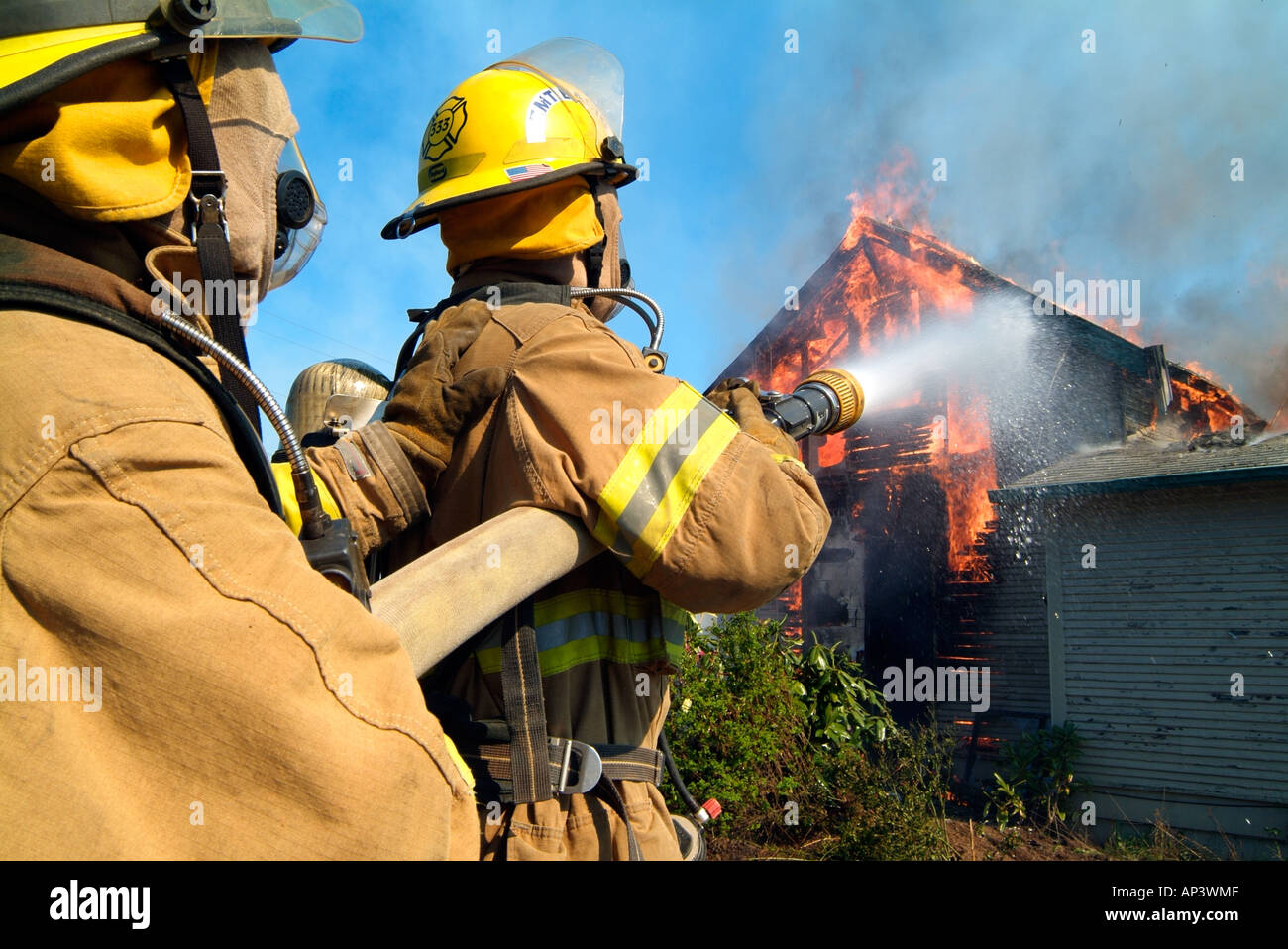Due vigili del fuoco versare l'acqua su un inferno, il tentativo di abbattere le fiamme che stanno consumando una casa. Foto Stock