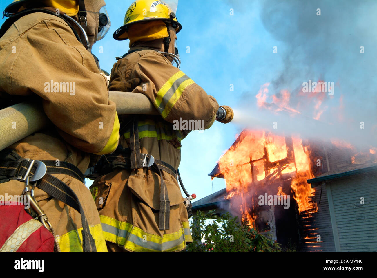 Due vigili del fuoco versare l'acqua su un inferno, il tentativo di abbattere le fiamme che stanno consumando una casa. Foto Stock