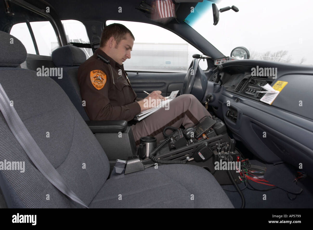 Vice Sheriff in cruiser scrivendo un biglietto di traffico e utilizzo di radio portatile per verificare la validità della patente di guida. Foto Stock