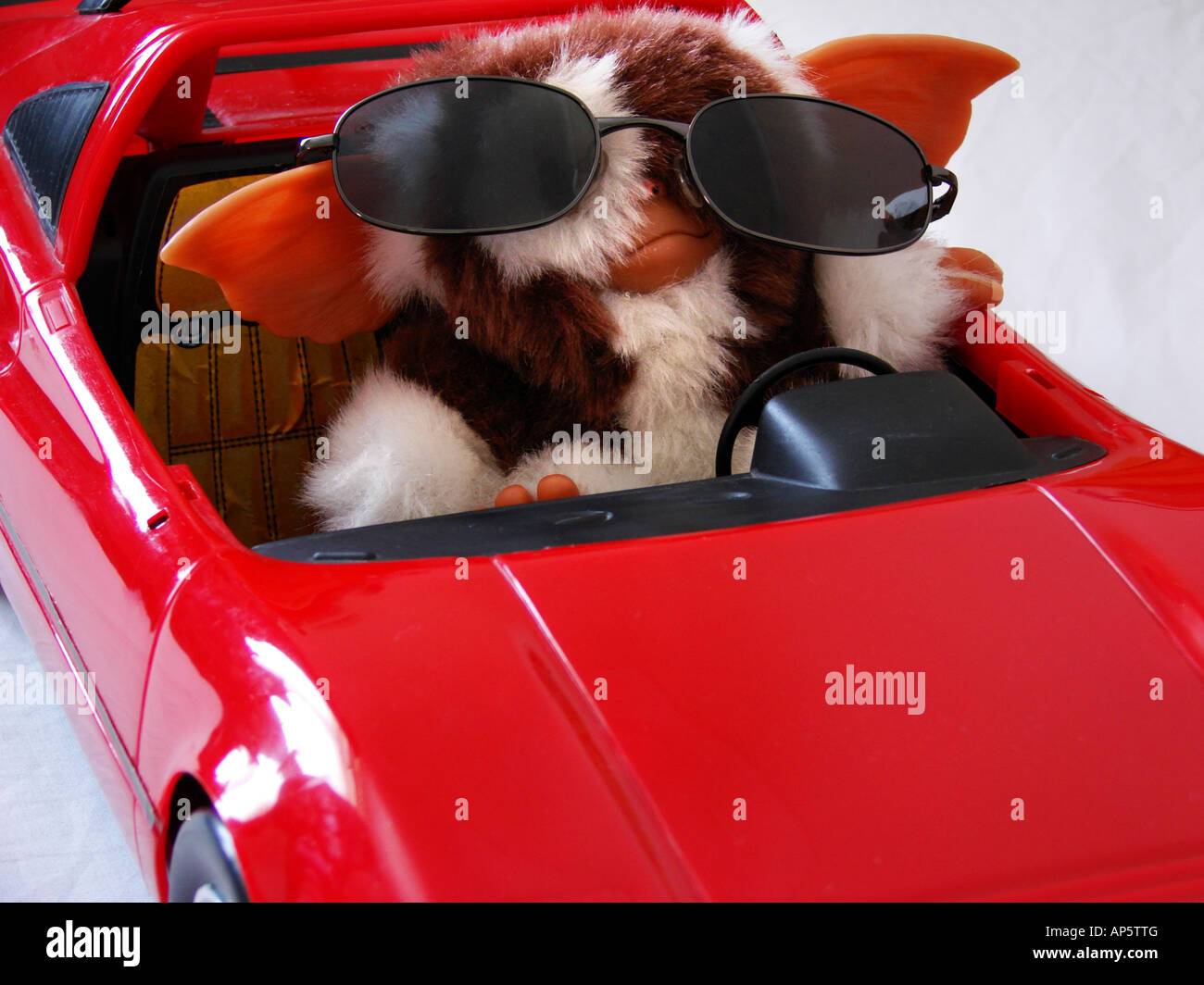 Gizmo il Gremlin alla guida di una automobile rossa indossando Sunglasse's Foto Stock