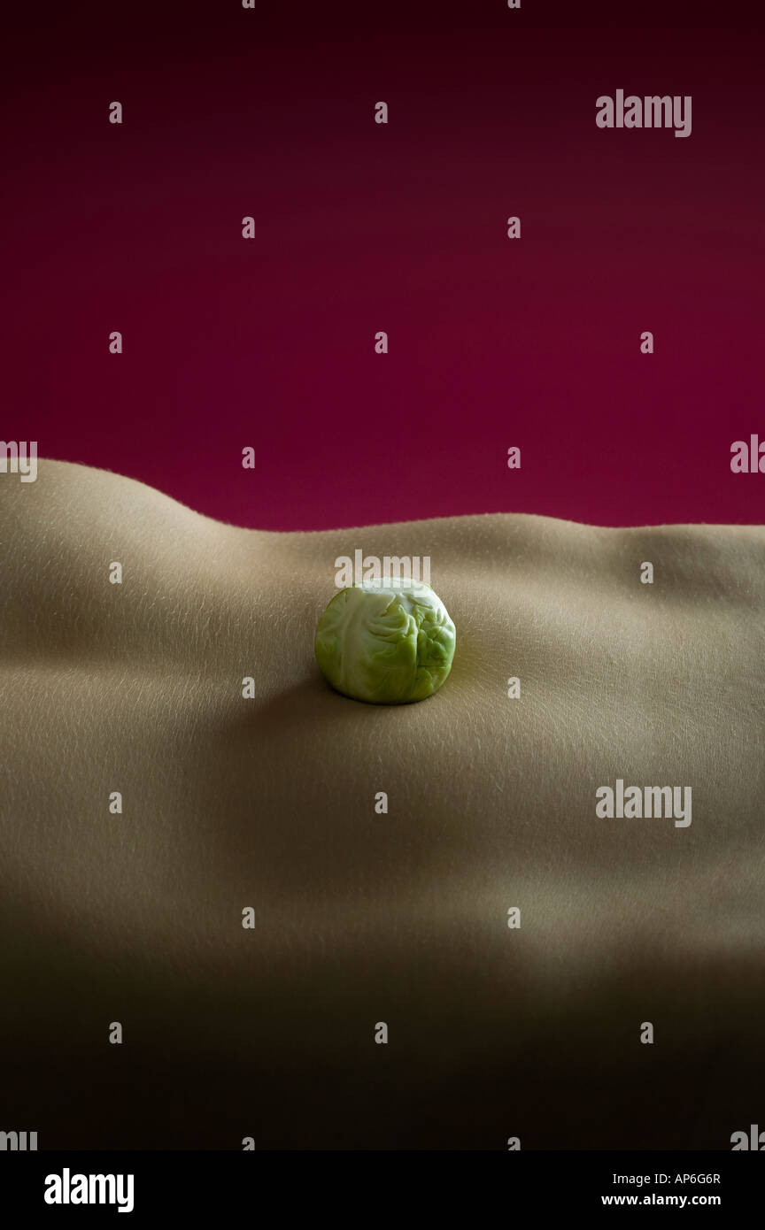 Unico germoglio di Bruxelles bilanciato su womans stomaco nudo Foto Stock
