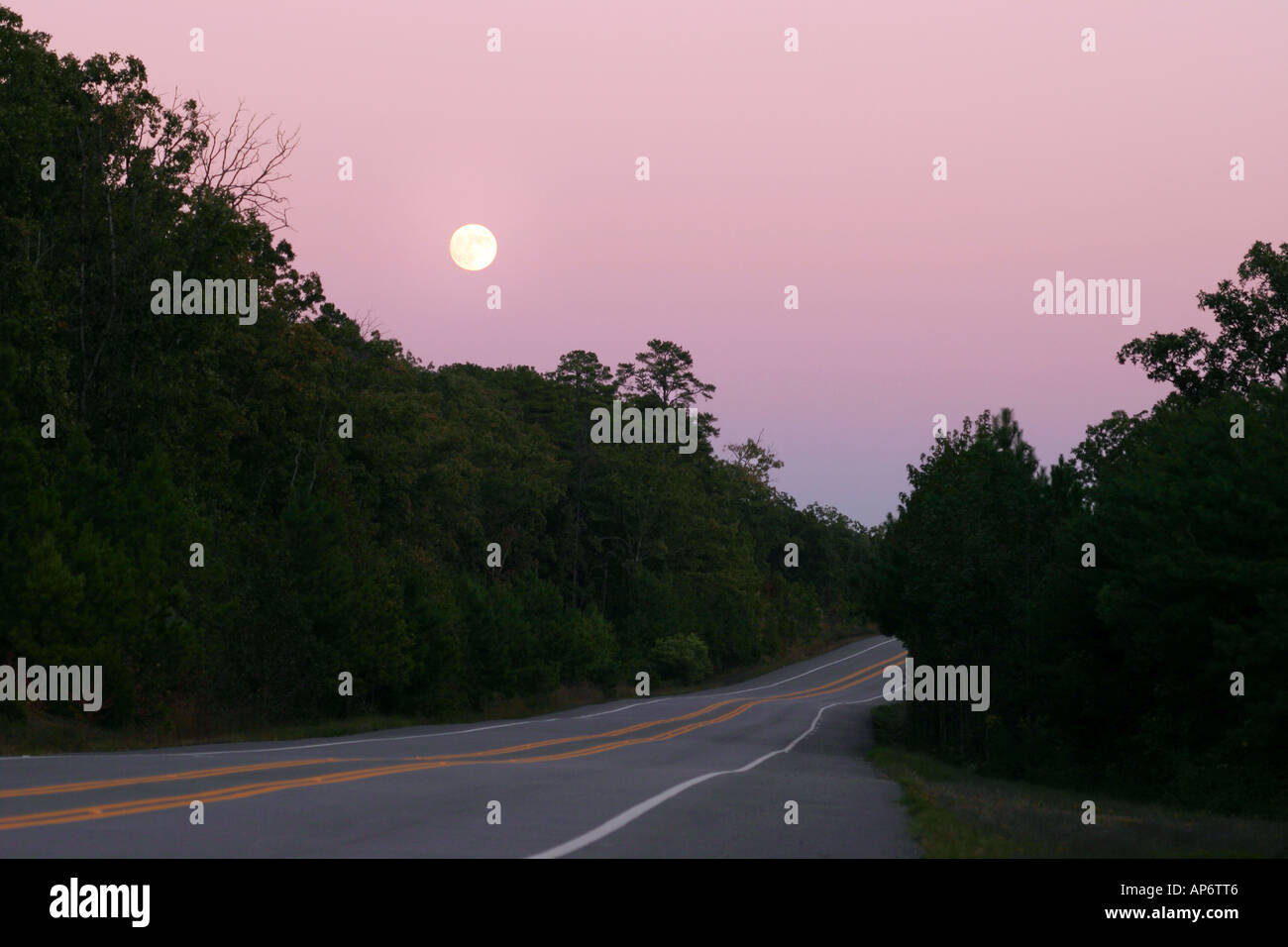 Strada asfaltata al tramonto con il sorgere della luna Foto Stock