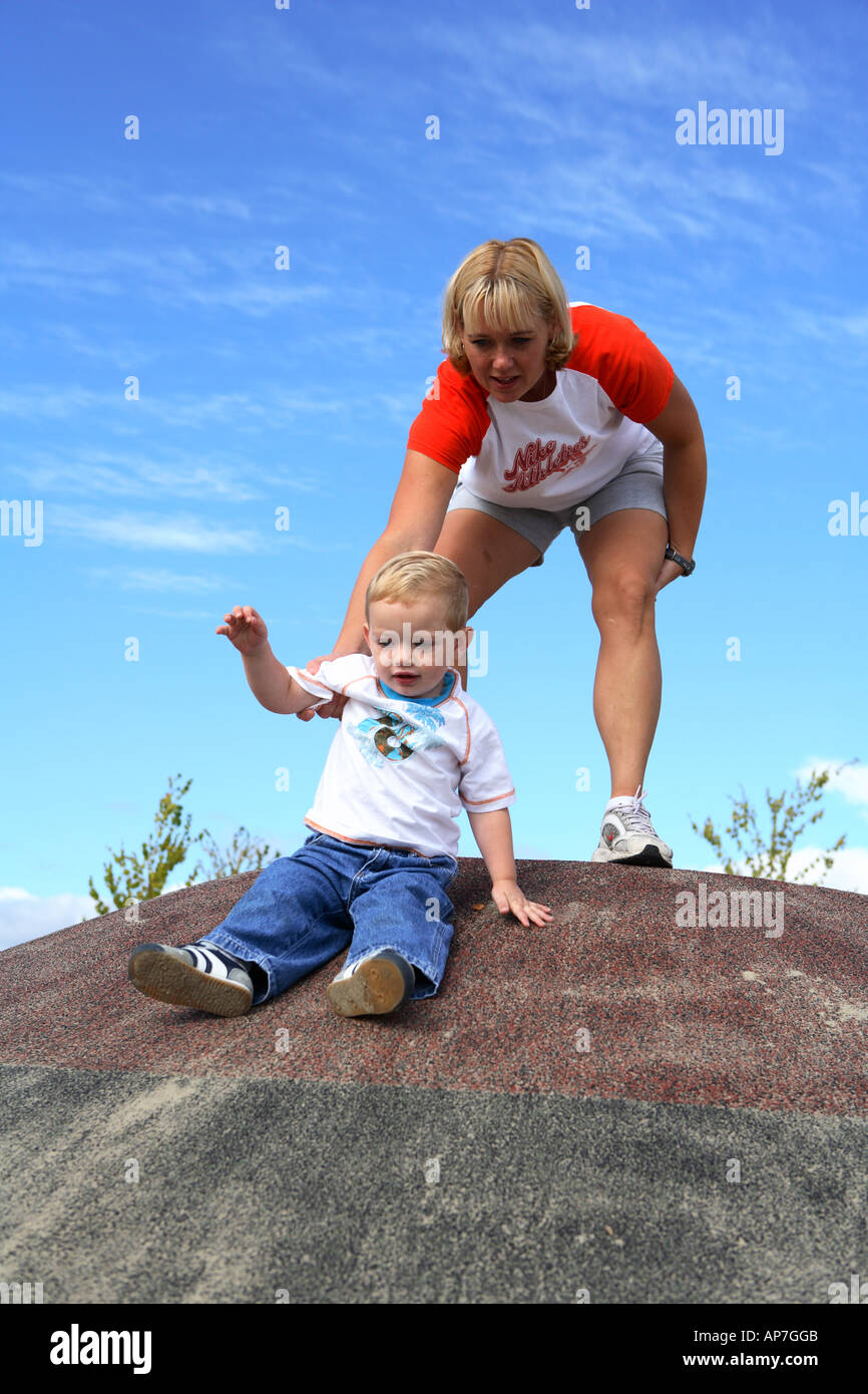 Mom aiutando figlio di due anni scorrere giù per la collina Foto Stock