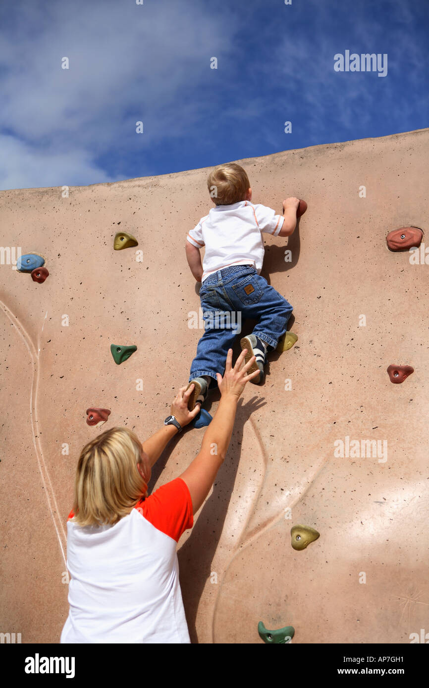 Mom per aiutare due anno vecchio ragazzo salire su una parete di roccia Foto Stock