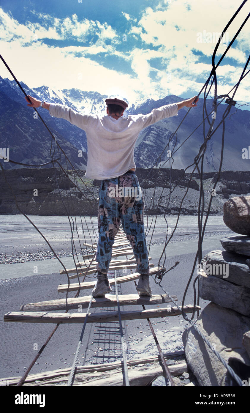 Viaggiatore intrepido attraversando il fiume Hunza sulla passerella sospesa Trekking nr Passu Karakoram Highway N Pakistan Foto Stock