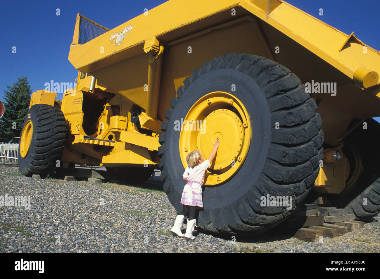 Rilasciato ragazza raggiungendo fino enorme ruota del trattore World Museum of Mining Butte Montana Foto Stock