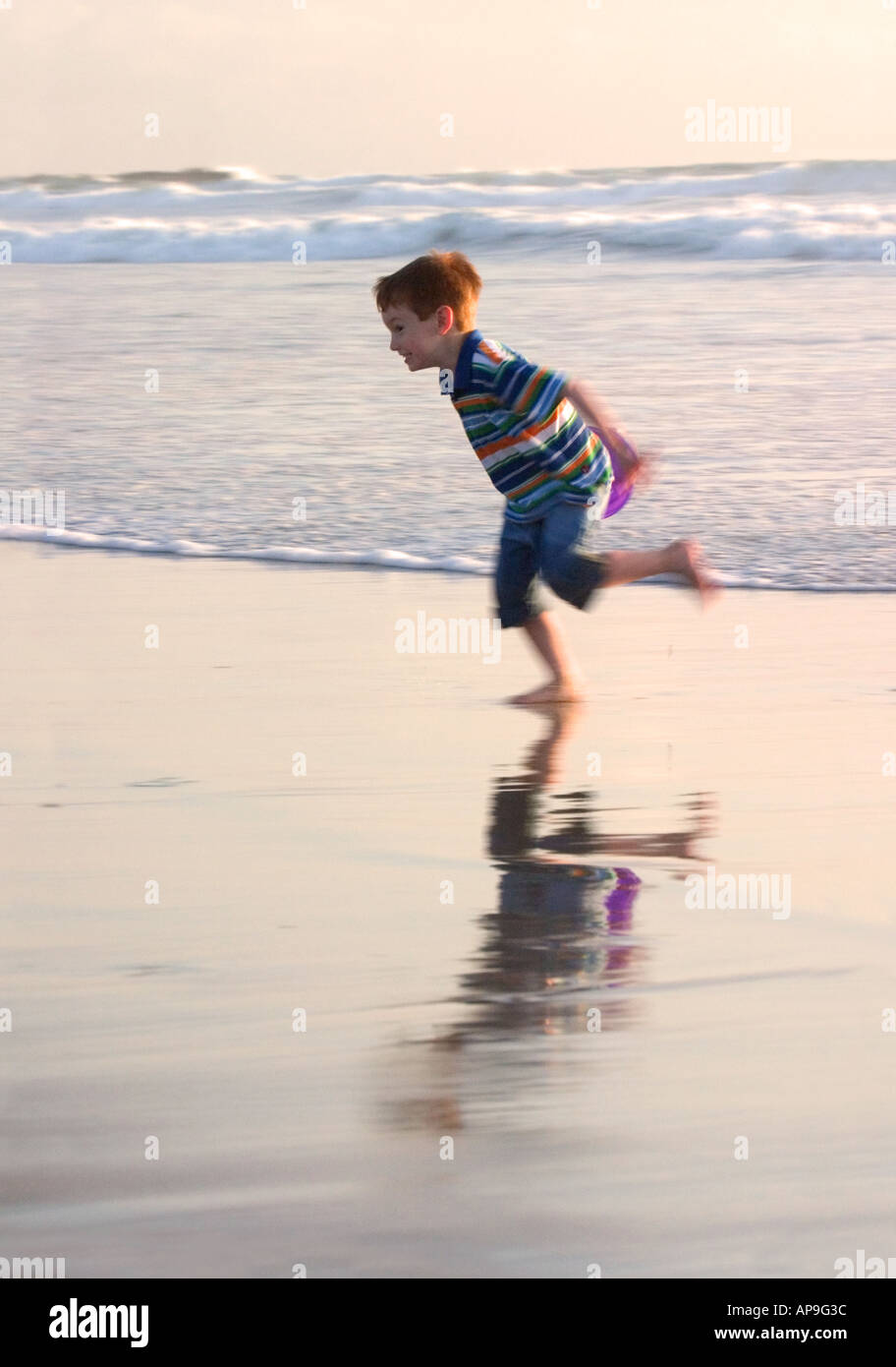 Un giovane ragazzo ride e corre dalle onde sulla spiaggia. Foto Stock