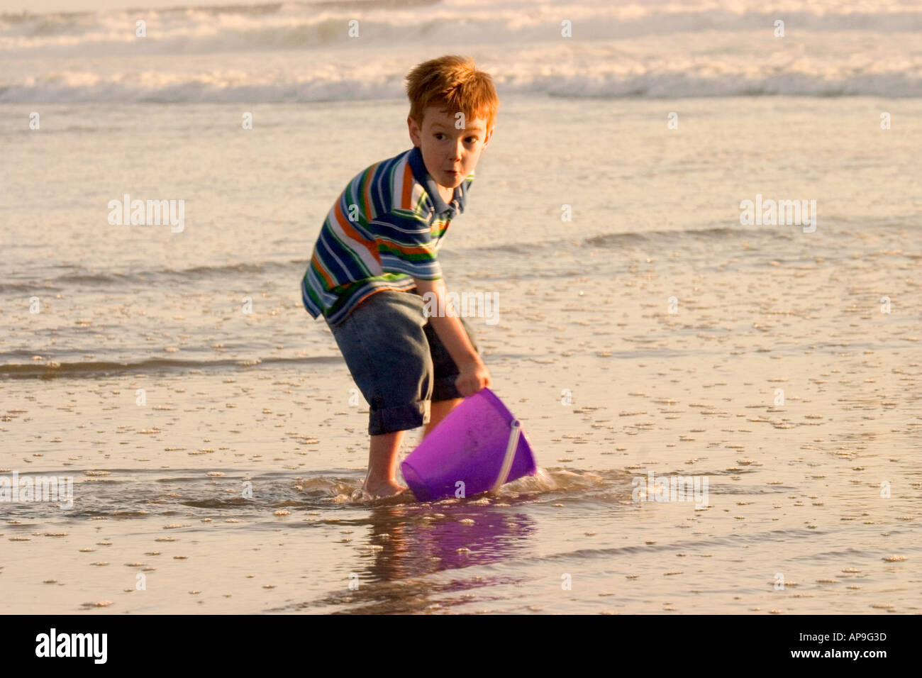 Un felice ragazzo mostra il suo compiacimento per la riproduzione in acqua sulla spiaggia. Foto Stock
