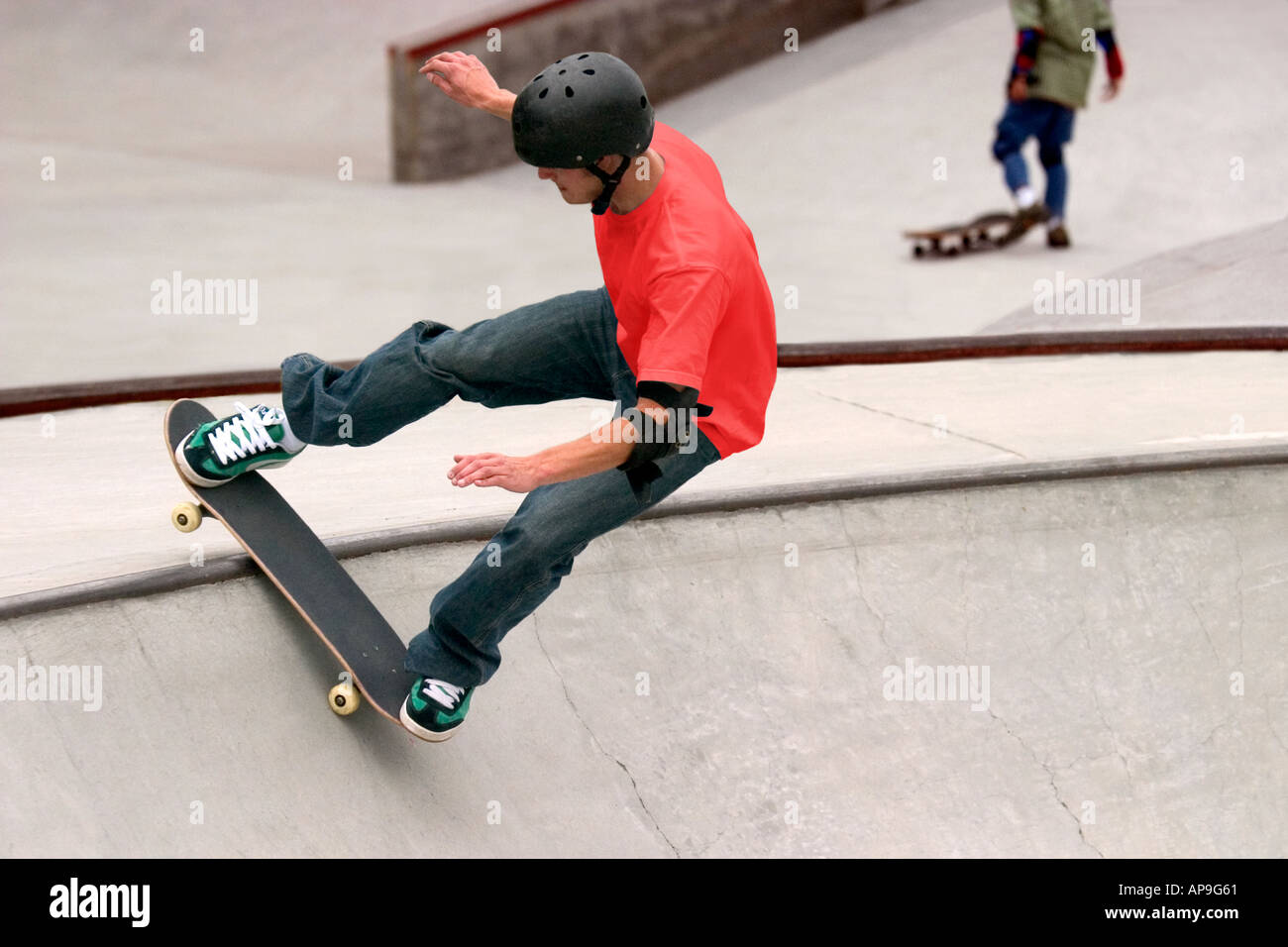 Un fermo immagine di azione di un giovane appassionato di skateboard a skate park, con una seconda skater in background. Foto Stock