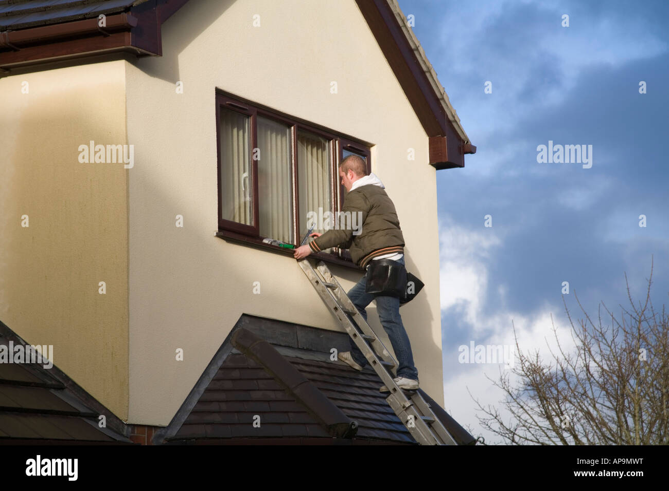 Il Galles del Nord Regno Unito un giovane uomo di pulizia della parte superiore delle finestre di un ambiente domestico Foto Stock