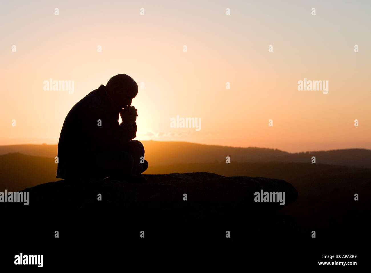 Profilo di Silhouette di un uomo seduto a pensare su di una collina a sunrise Foto Stock