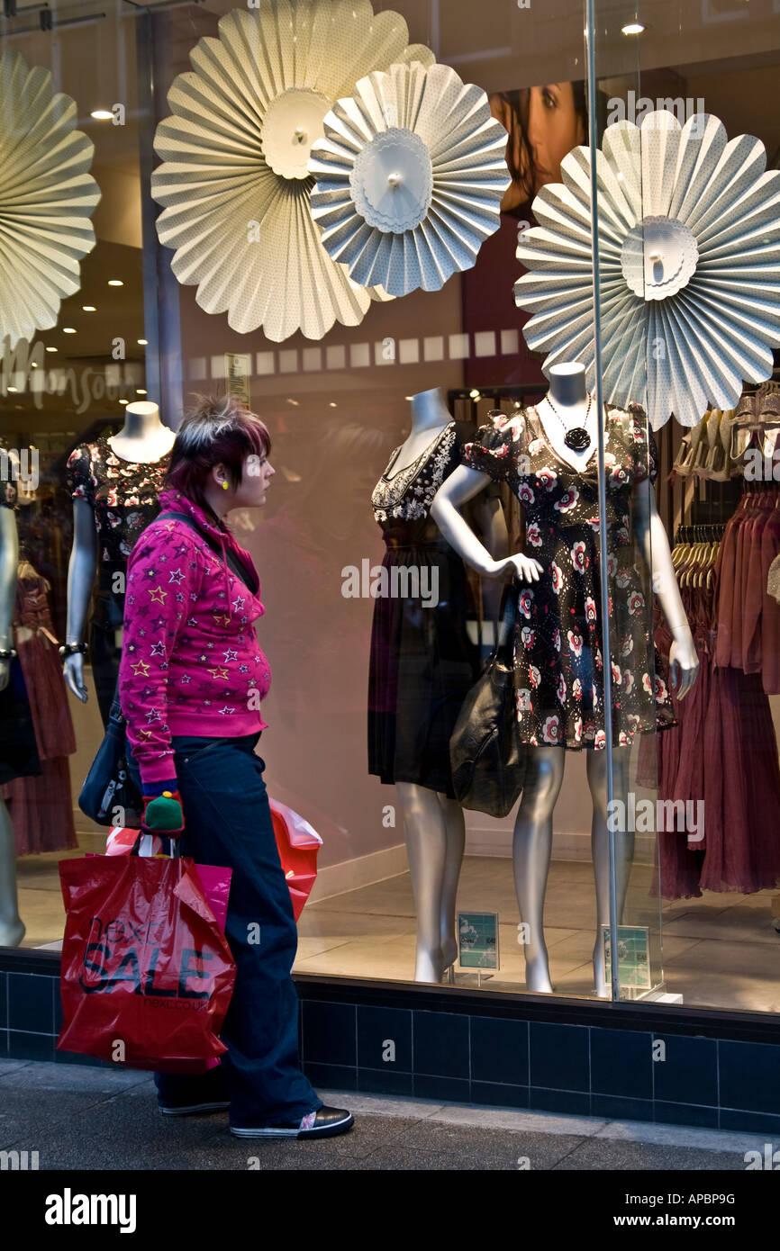 Una femmina di shopper che trasportano i sacchetti di plastica in piedi di fronte a un negozio di moda vetro durante il mese di gennaio le vendite a Dundee, Regno Unito Foto Stock