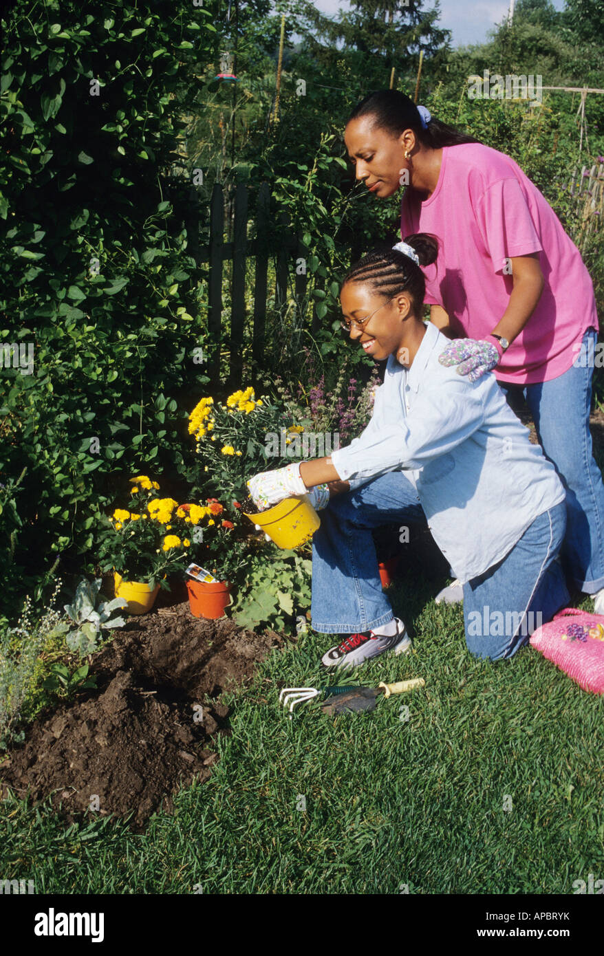 Madre e figlia piantare fiori OHIO USA famiglia hobby giardinaggio recinzione relazioni estate americano africano donne Foto Stock