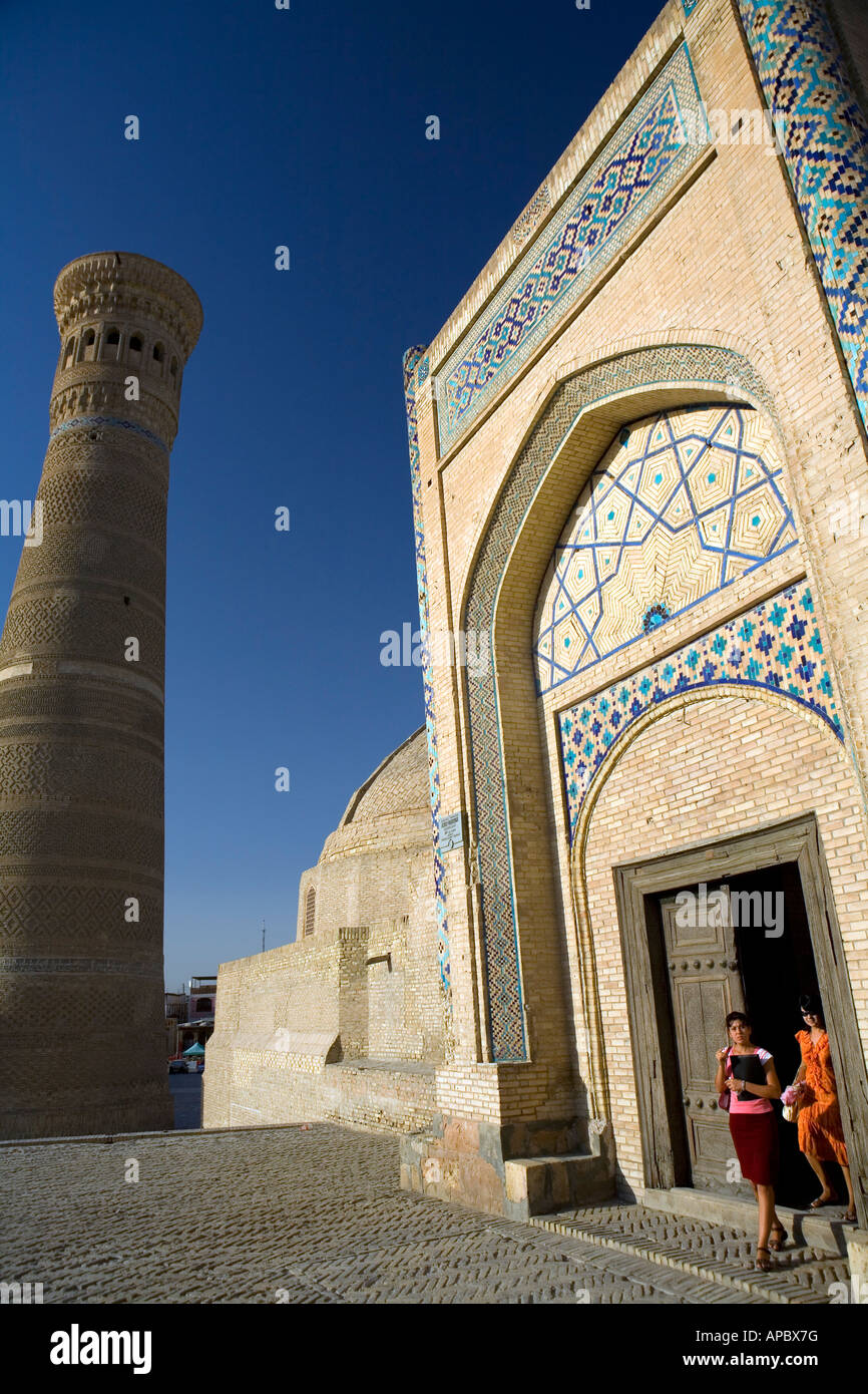 Le donne di uscire da Amir Alim Khan Madrassa con minareto Kalon dietro Foto Stock