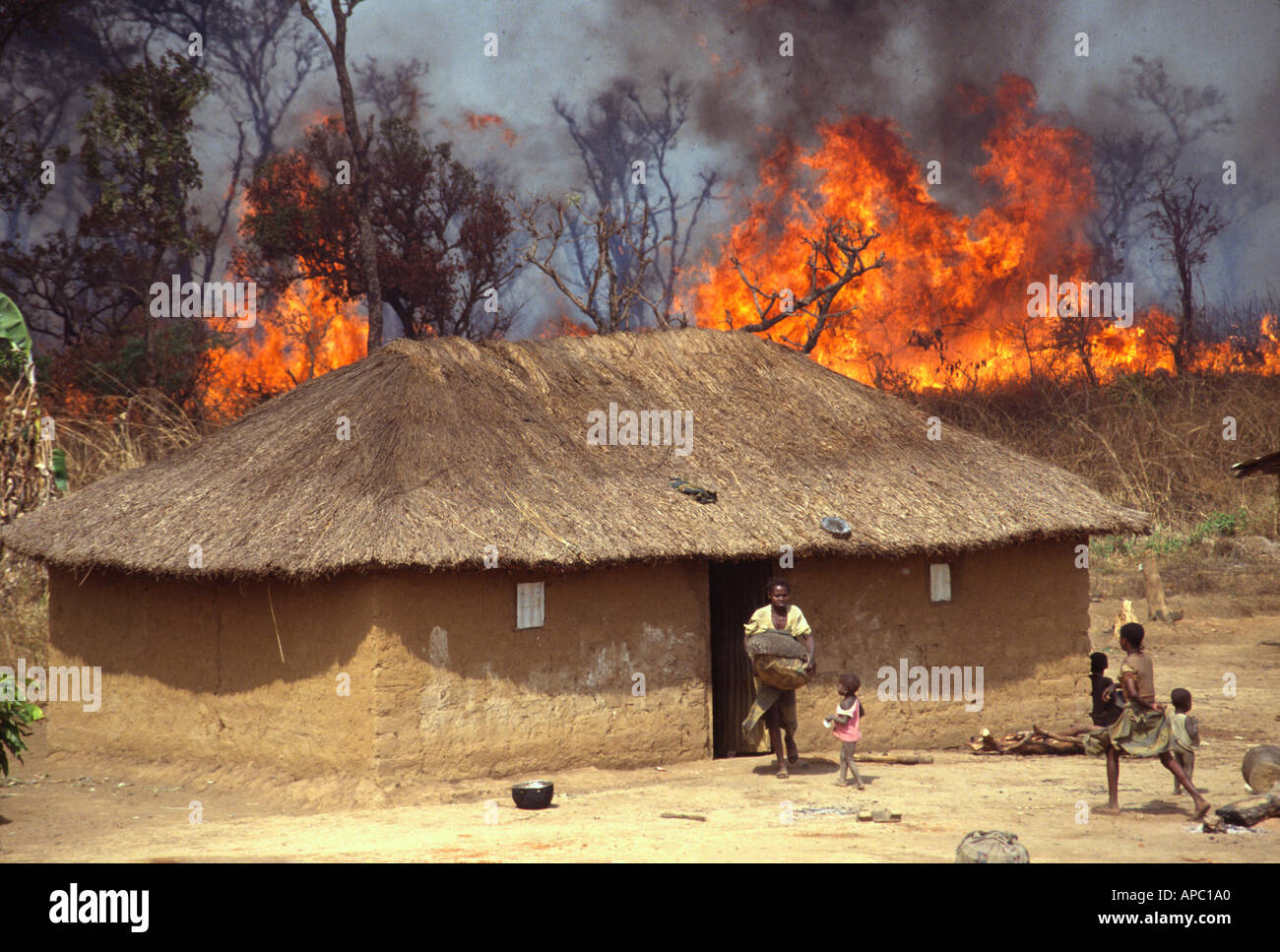 Una famiglia sfugge come il fuoco si avvicina con tetto di paglia di una capanna di fango Nella Repubblica Centrale Africana Foto Stock