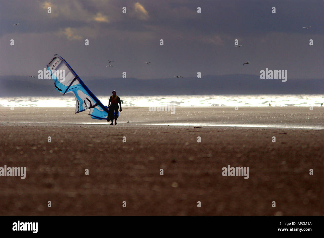 Un kitesurfer passeggiate fino alla spiaggia in un tardo pomeriggio invernale come il sole si rompe a ovest, Ainsdale, UK. Foto Stock
