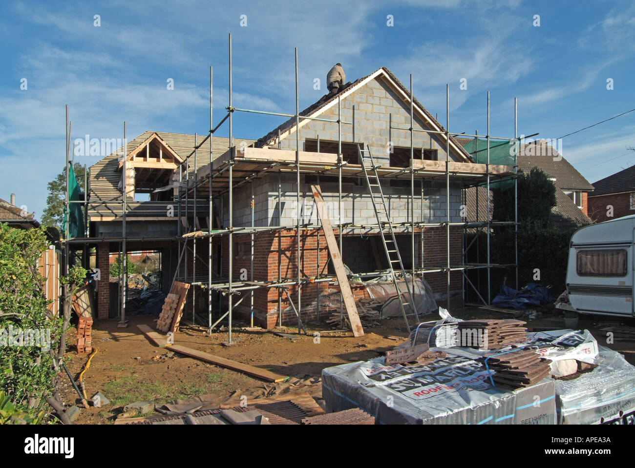 Terreno edificabile con casa indipendente in costruzione e lavori in corso con piastrellatrice del tetto in funzione in una fredda giornata invernale 3xyz Essex Inghilterra Regno Unito Foto Stock